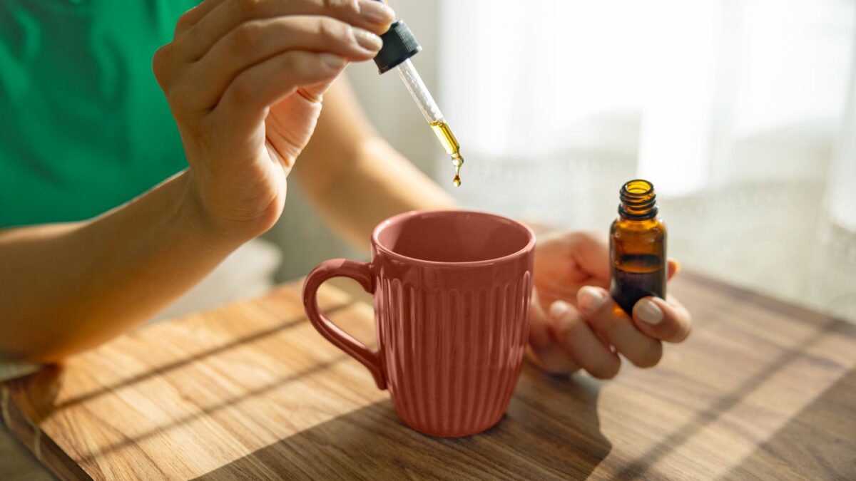 Choose the Right CBD Product - A person adding CBD oil drops to a cup of tea or coffee using a dropper and amber tincture bottle.