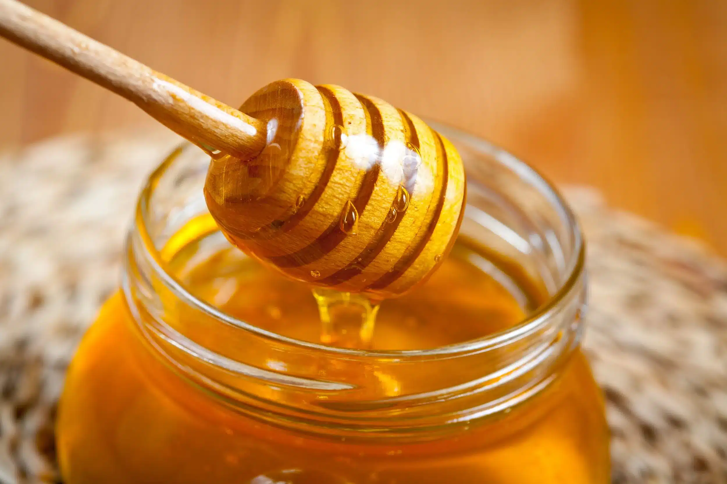 Close-up of organic honey dripping from a wooden honey dipper into a glass jar, showcasing natural honey benefits for CBD honey products from TheCannaCompany.com