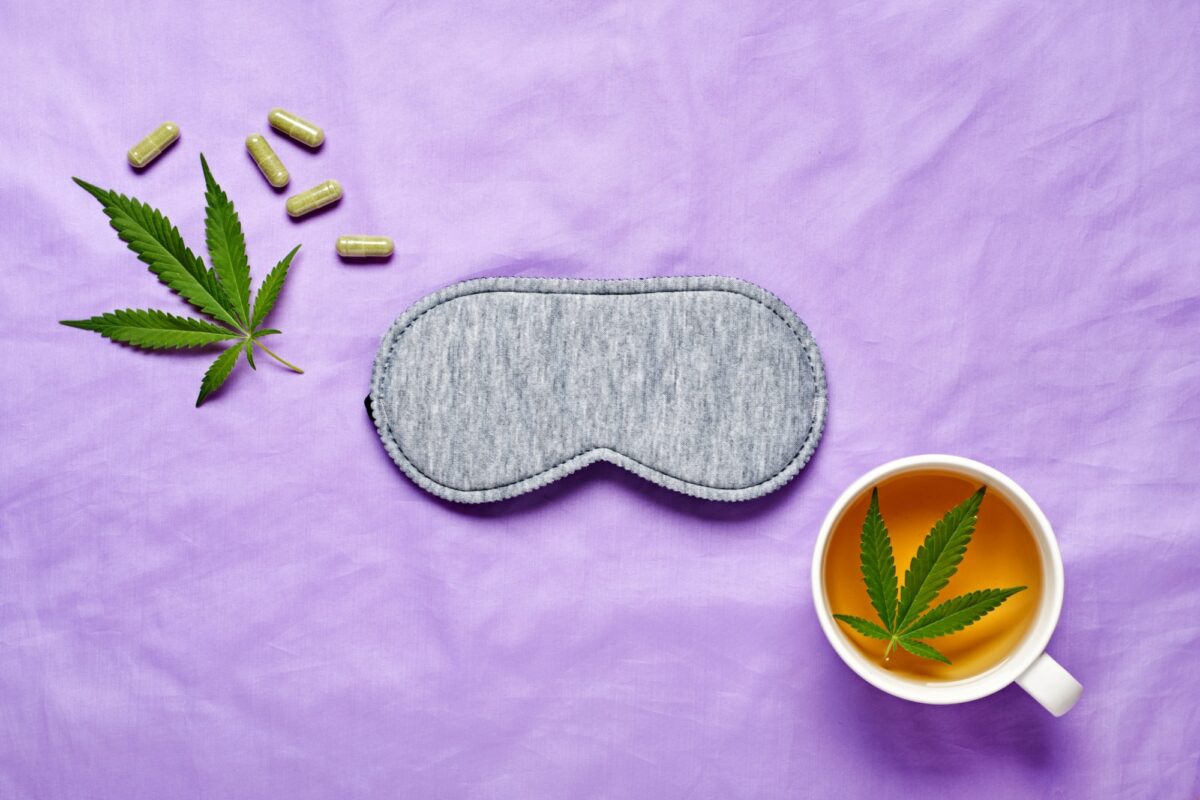 CBD sleep aids with cannabis leaf, herbal capsules, eye mask, and tea on purple background