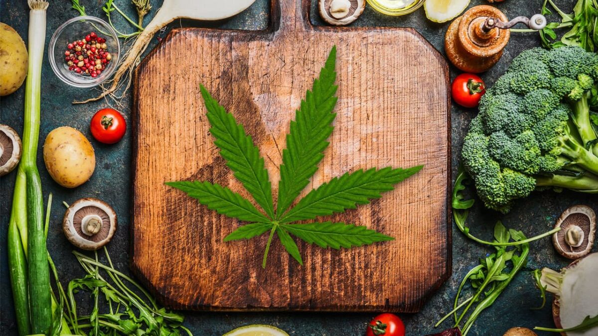 Fresh vegetables and a wooden cutting board with a hemp leaf, symbolizing cooking with CBD, CBG, and THCa tinctures.
